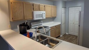 A kitchen with wooden cabinets, a white microwave, a stainless steel sink, and a refrigerator.