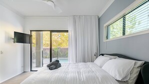 Un dormitorio con una cama grande, un televisor montado en la pared y un ventanal corredero que da a un espacio al aire libre.