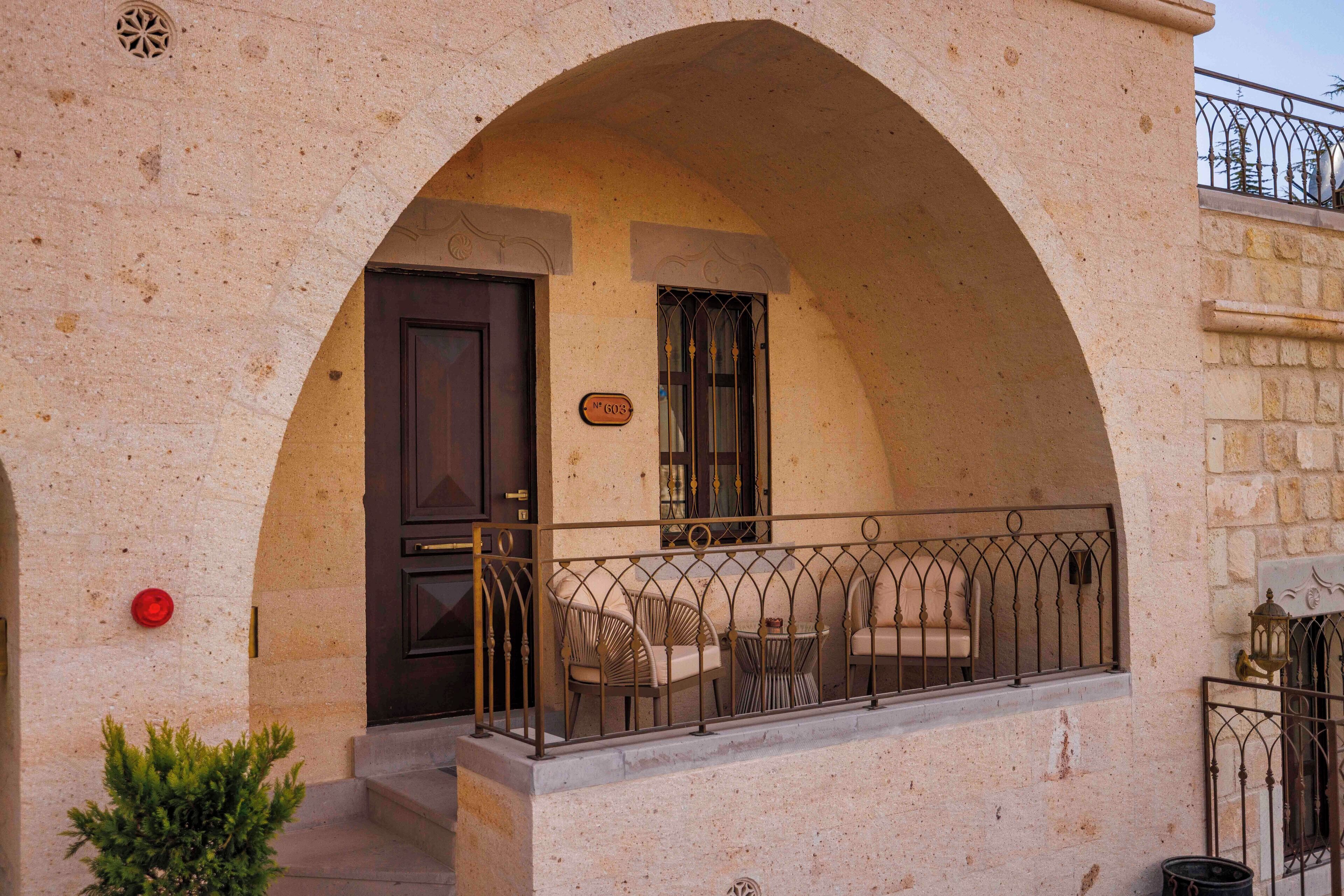 A building with a stone facade, an arched entrance, a balcony with metal railings, and a small potted plant.