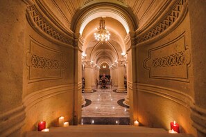 Un amplio pasillo con candelabro, pisos de mármol y mesas iluminadas con velas.