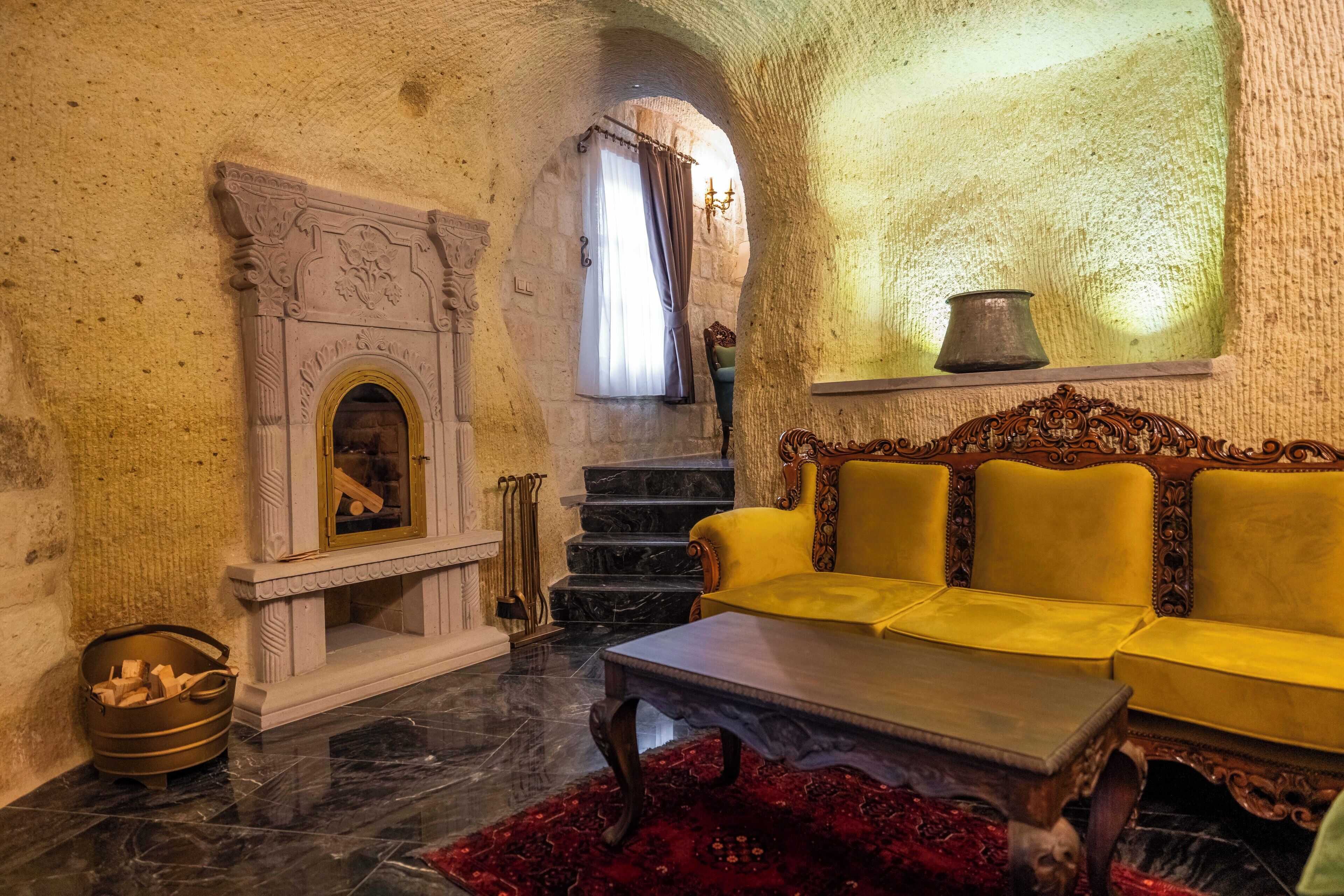 A room with a fireplace, a yellow sofa, a red rug, and a staircase leading to an upper level.