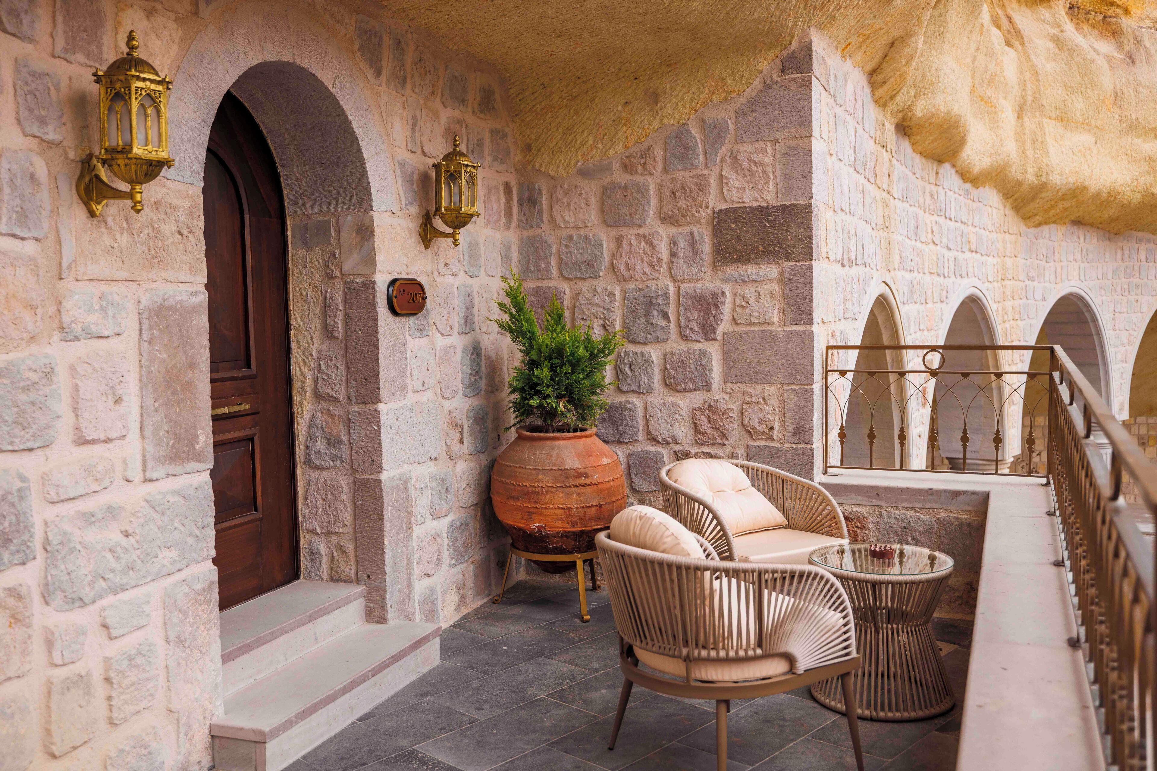 Un espacio al aire libre con paredes de piedra, muebles de mimbre y una maceta grande de terracota.