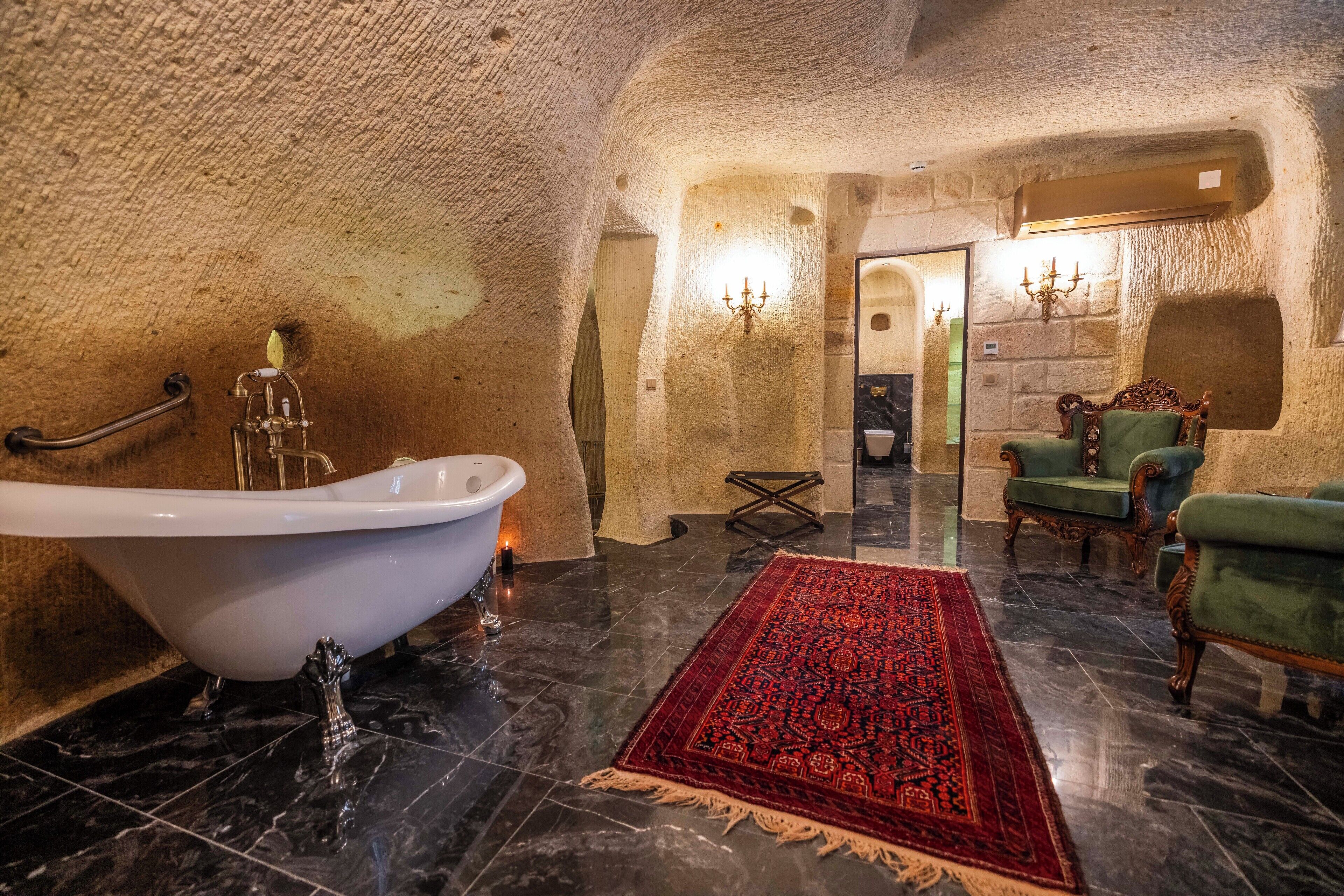 Una habitación con una bañera, una alfombra roja estampada y sillones tapizados en verde.
