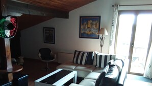 Una sala de estar con sofá, una mesa de centro y una lámpara. Hay un cuadro en la pared y una ventana con cortinas.