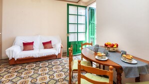 A cozy room with a patterned floor, a wooden dining table with plates of food, a green door, and a white sofa with red cushions. - Apartment Baldri by Interhome (Tossa de Mar)