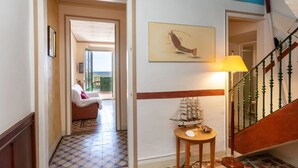 A hallway with a tiled floor, a staircase with green railings, and a painting of a fish. - Apartment Baldri by Interhome (Tossa de Mar)