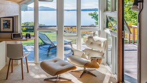 A modern room with a large window, a wooden ceiling, and a view of a lake. - Oak Point Bluff! Oceanfront! (Trenton)