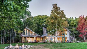 A modern house with a large deck, stone chimney, and a well-maintained lawn. - Oak Point Bluff! Oceanfront! (Trenton)