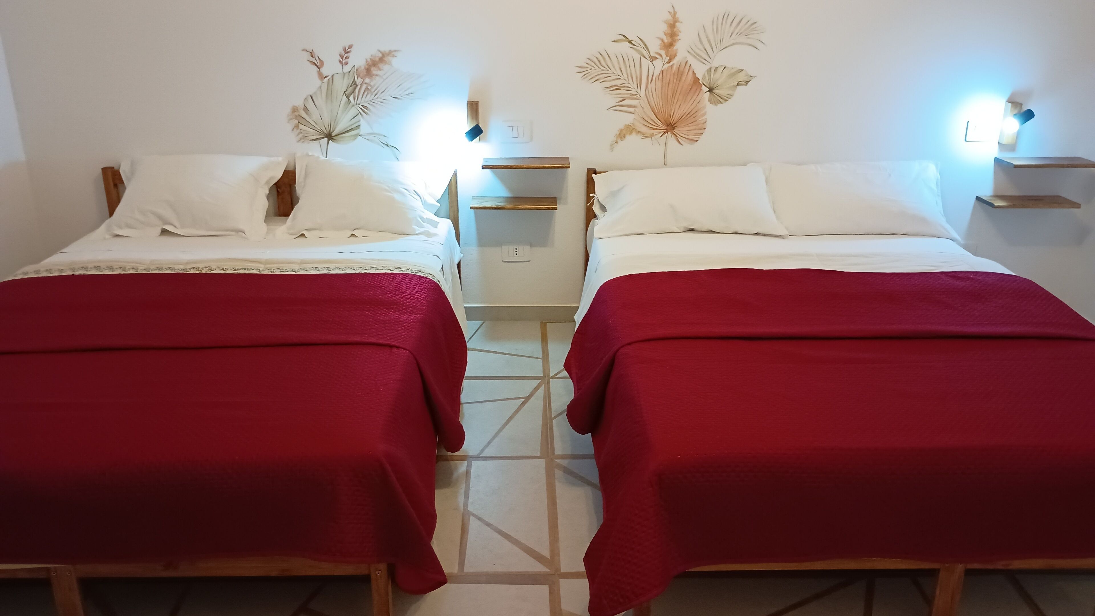 Two single beds with red bedspreads, white pillows, and decorative wall art.