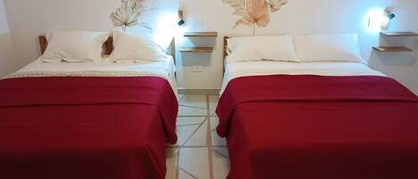 Two single beds with red bedspreads, white pillows, and decorative wall art.