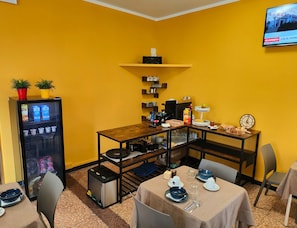 A dining area with a yellow wall, a vending machine, a coffee machine, and a clock. - Albergo Astoria Loano  (Loano)