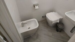 Ein kleines, modernes Badezimmer mit weißen Fliesen, einem Bidet, einer Toilette und einem Waschbecken.
