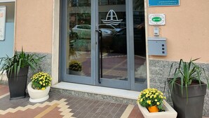 Das äußere Erscheinungsbild des Hotels Albergo Astoria, mit einem blauen Schild mit dem Hotelnamen, einer Rezeption und mehreren Flaggen.
