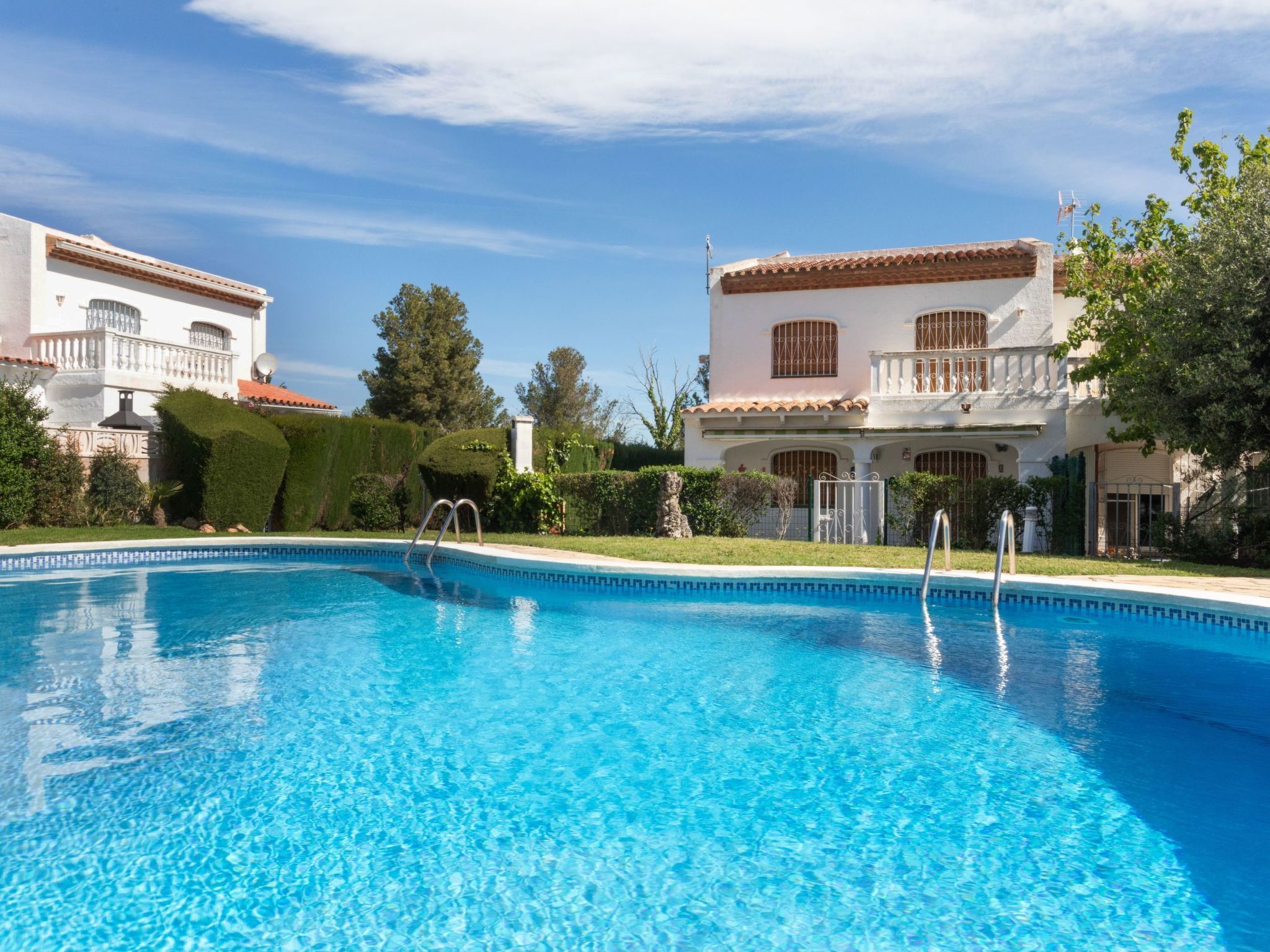 Une piscine à l’eau d’un bleu cristallin, entourée de bâtiments blancs aux toits recouverts de tuiles rouges et dotés de balcons.