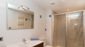 Un baño moderno con un espejo grande, un lavamanos, un inodoro y una ducha con mampara de vidrio.