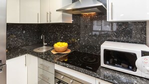 Una cocina moderna con armarios blancos, encimera de granito negro, campana extractora de acero inoxidable, microondas integrado y estufa a gas.