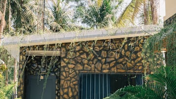 Un edificio con fachada de piedra, una puerta oscura y un pequeño jardín con palmeras.