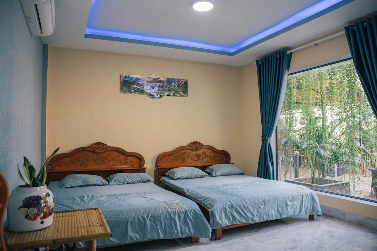 A room with two wooden beds, a small table with a plant, and a window with curtains.