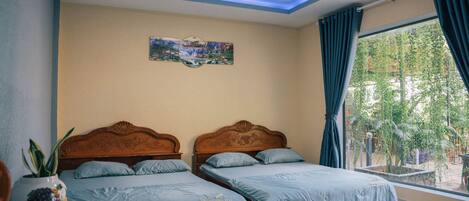 A room with two wooden beds, a small table with a plant, and a window with curtains.