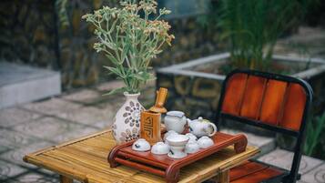 A table with a vase of flowers, a wooden tray with teapots, and a chair.