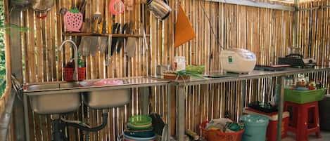 A kitchen with a bamboo wall, stainless steel sinks, and various kitchen utensils and appliances.
