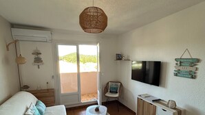 Een woonkamer met een bank, een klein rond tafeltje, een televisie en een plafondventilator.