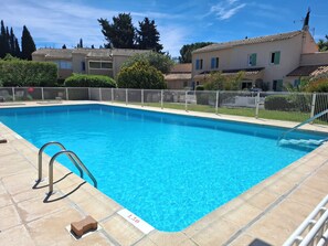 Une piscine d’un bleu éclatant, avec un escalier en métal, entourée d’une clôture, et des immeubles d’habitation en arrière-plan.