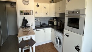 Een compacte keuken met witte kastjes, een wasmachine, een magnetron en een koelkast.