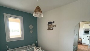 Een slaapkamer met een bed, een raam, een hanglamp en een wanddecoratie.