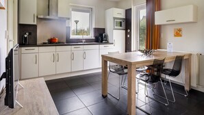 A modern kitchen with white cabinets, a wooden dining table, and black chairs. - Bungalowpark It Wiid by Interhome (Eernewoude)