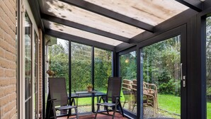 A sunroom with a glass door, a wooden deck, and a round table. - Bungalowpark It Wiid by Interhome (Eernewoude)