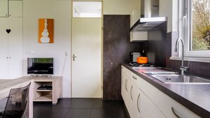 A modern kitchen with a stove, sink, and cabinets. There is a television and a door with a frosted glass window. - Bungalowpark It Wiid by Interhome (Eernewoude)