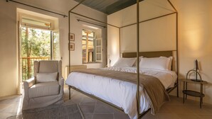 A bedroom with a four-poster bed, a chair, a small table, and a view of the outdoors. - Casa Oliva (Treis Elies)