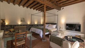 A room with a bed, a dining table, chairs, a TV, and a stone wall. - Casa Oliva (Treis Elies)