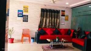 A living room with a red sofa, black cushions, a small table with a plant, and motivational posters on the wall. - Way Inn Familiar (Hyderabad)