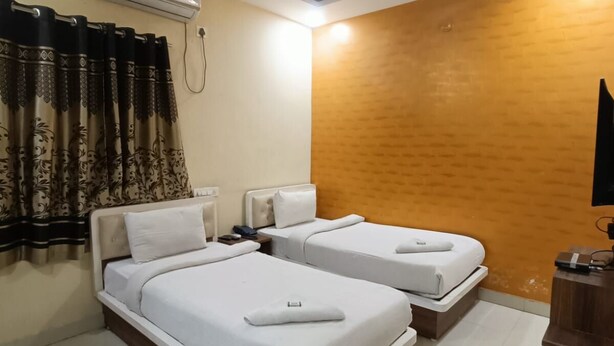 A hotel room with two beds, an air conditioning unit, a ceiling fan, a wooden accent wall, and a small wooden desk. - Way Inn Familiar (Hyderabad)