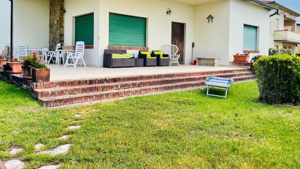 A modern house with a covered patio, outdoor seating, and a well-maintained lawn.
