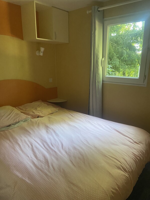 Een slaapkamer met een bed, een raam met gordijnen, een nachtkastje en een spiegel aan de muur.