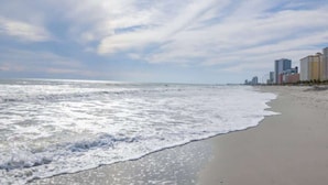 A beach with waves and a city skyline in the background. - King Suite, Kitchen, New HVAC, Ocean Views, Walk to Attractions & Restaurants (Myrtle Beach)