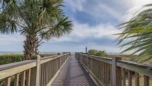 A wooden boardwalk leading to the beach, surrounded by palm trees and a clear sky. - King Suite, Kitchen, New HVAC, Ocean Views, Walk to Attractions & Restaurants (Myrtle Beach)