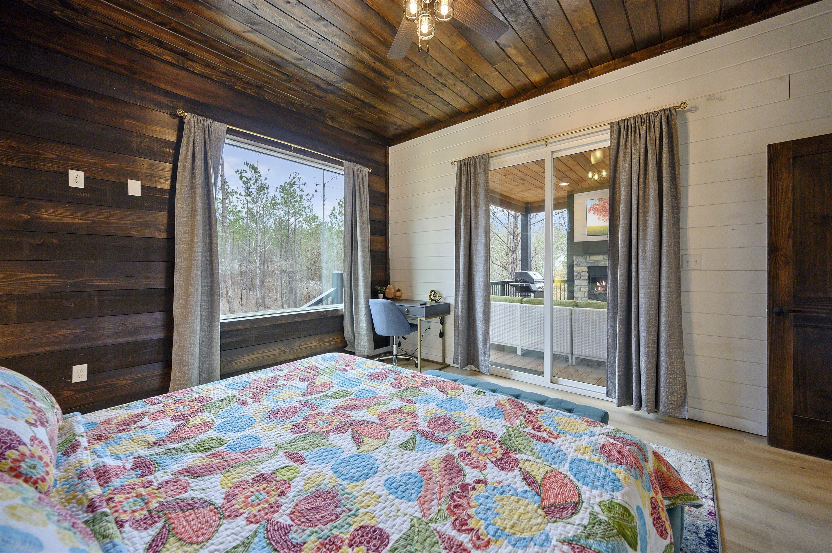 A bedroom with a large bed, a desk, and a view of the outdoors.