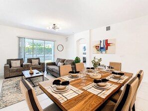 A modern living room with a dining area, large windows, and a contemporary art piece.