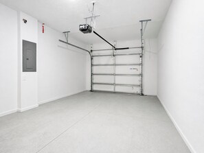 Un garage propre et vide, avec un projecteur fixé au plafond, un extincteur et une porte sur le côté gauche.