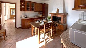 Eine Küche mit Holzschränken, einem Esstisch gedeckt mit Tellern und Gläsern, einem Kamin und einem Spülbecken.