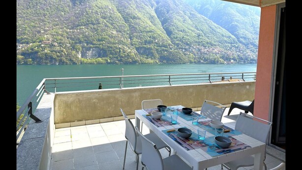 A balcony with a table set for dining, overlooking a lake with mountains in the background. - Riflessi sul Lago Apt Laglio - Tramonto (Laglio)