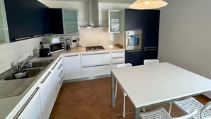 A modern kitchen with white cabinets, a stainless steel sink, a microwave, and a stove. There is a white dining table with four chairs. - Riflessi sul Lago Apt Laglio - Tramonto (Laglio)