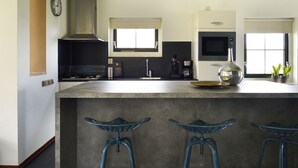 A modern kitchen with a large island, bar stools, a microwave, and a window. - Lieskehuis Wellness de Luxe 10+2 by Interhome (Vlagtwedde)