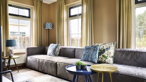 A modern living room with a grey sectional sofa, a small round table with a plant, and a lamp on a side table. - Lieskehuis Wellness de Luxe 10+2 by Interhome (Vlagtwedde)