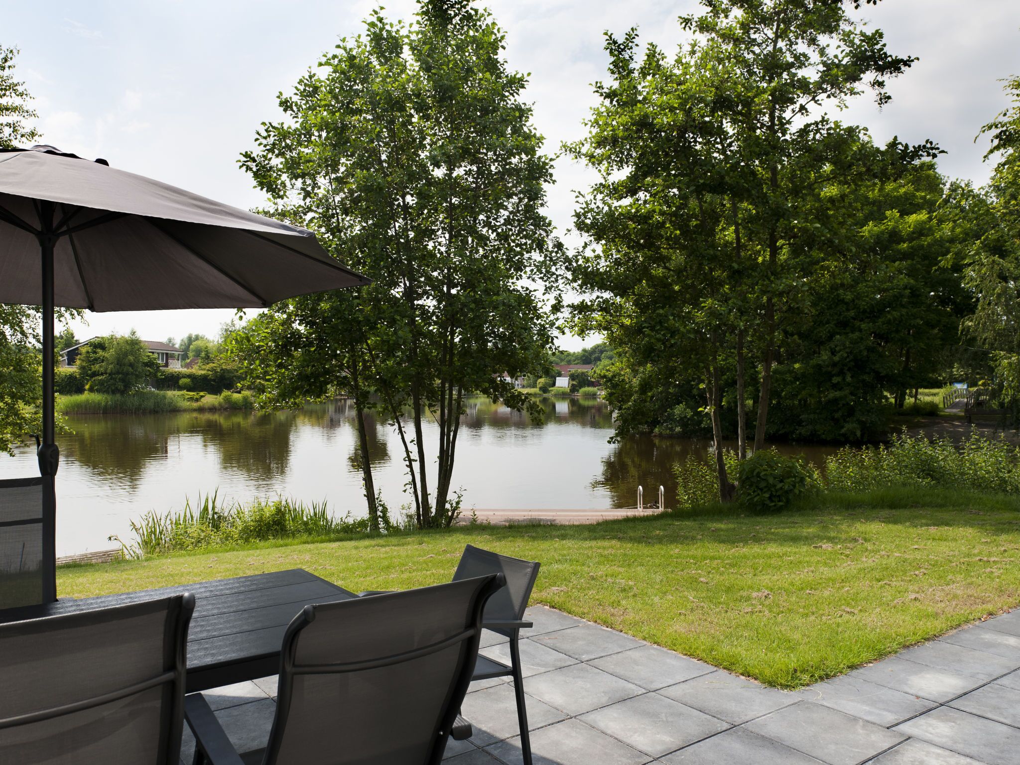 Eine Terrass mit Tisch und Stühlen, einem überdachten Bereich und Blick auf einen von Bäumen gesäumten See.