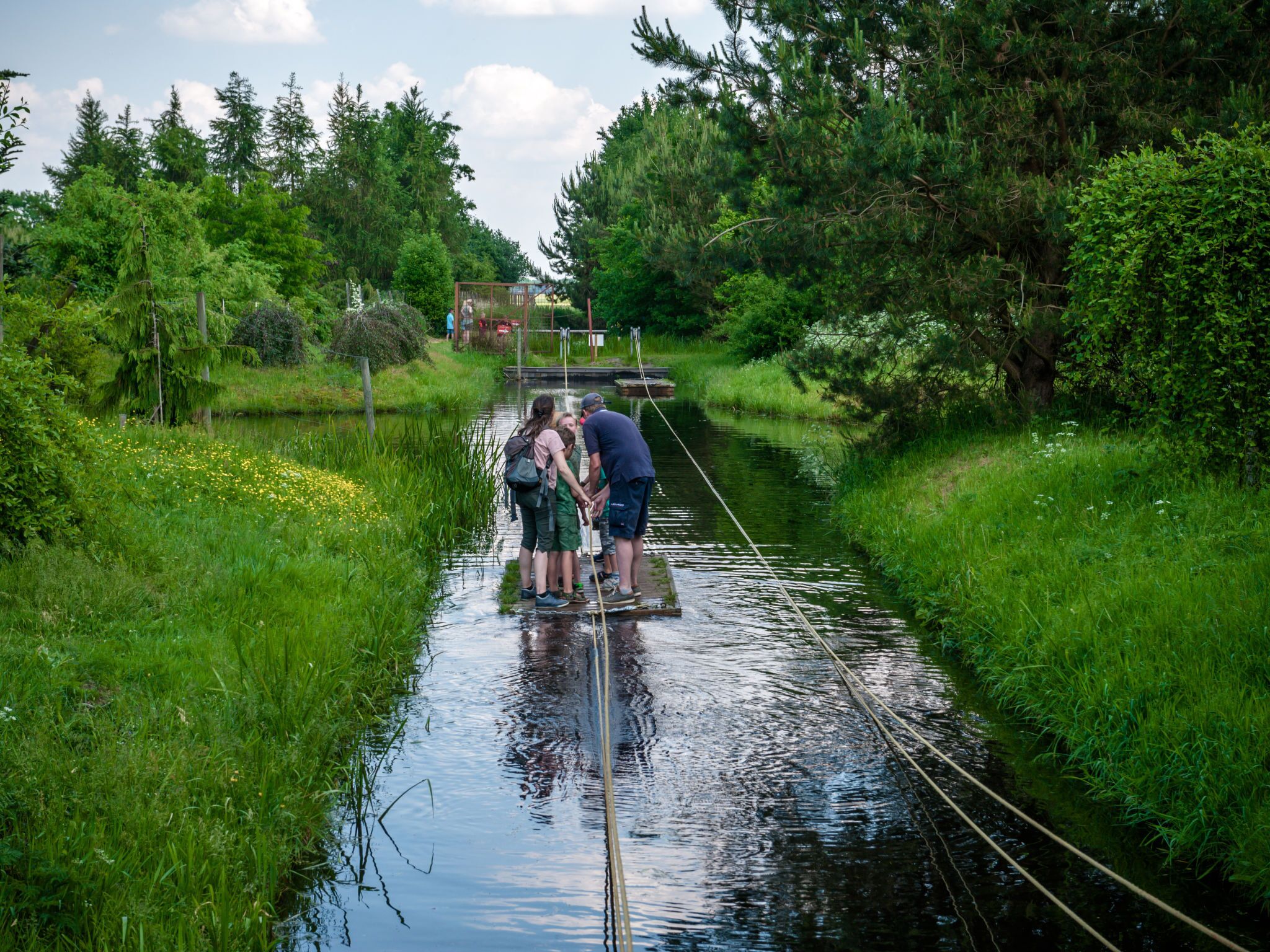 A narrow waterway with people crossing on a rope bridge.